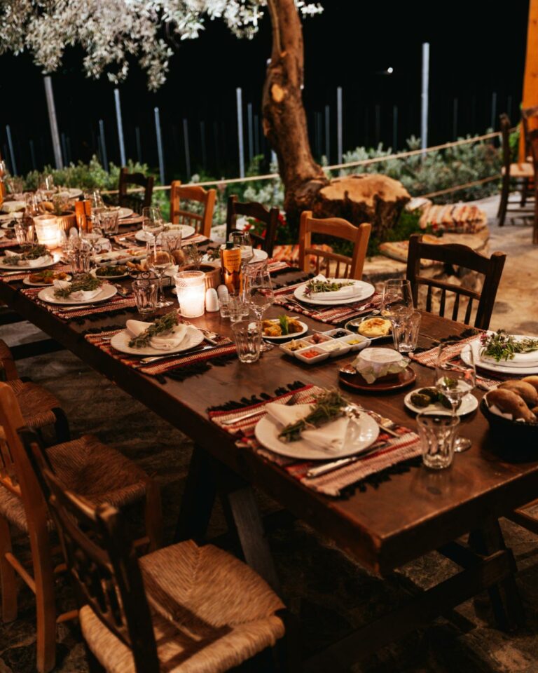 Outdoor dining table at Agreco Farm set with traditional Cretan dishes, plates, wine glasses and candles among the trees.