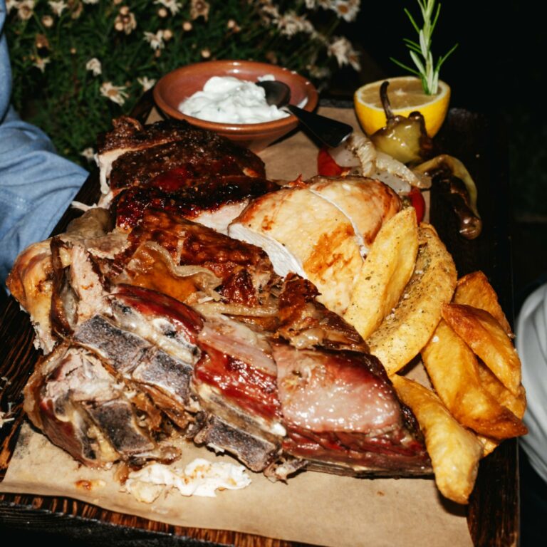 Platter of roasted meat served with potatoes and traditional Cretan side dishes.