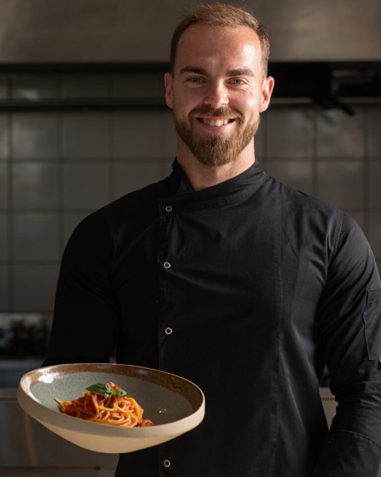 Chef holding a gourmet pasta dish at Brasserie Ariadne