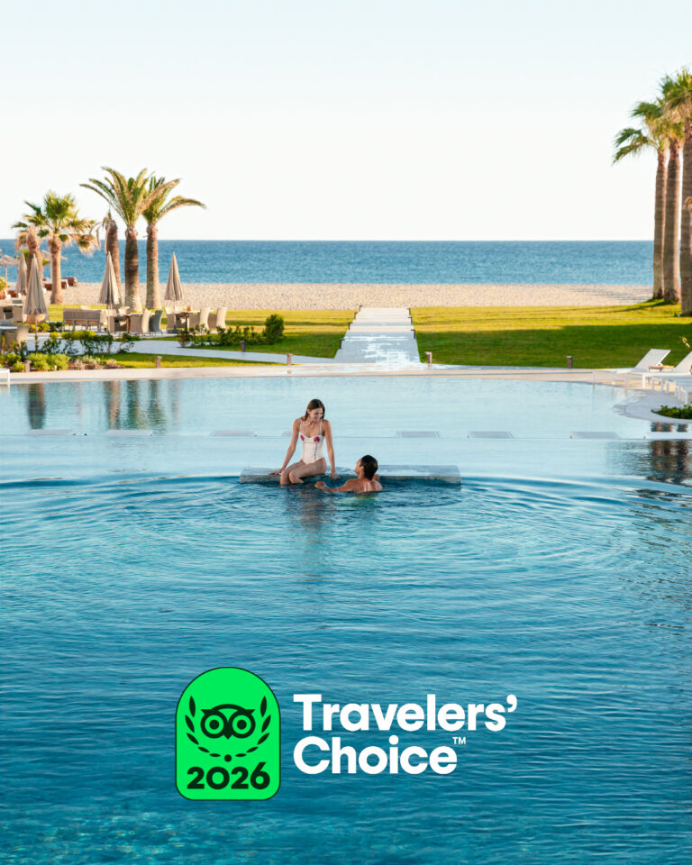 Outdoor swimming pools surrounded by palm trees and sun loungers at Grecotel Creta Palace.
