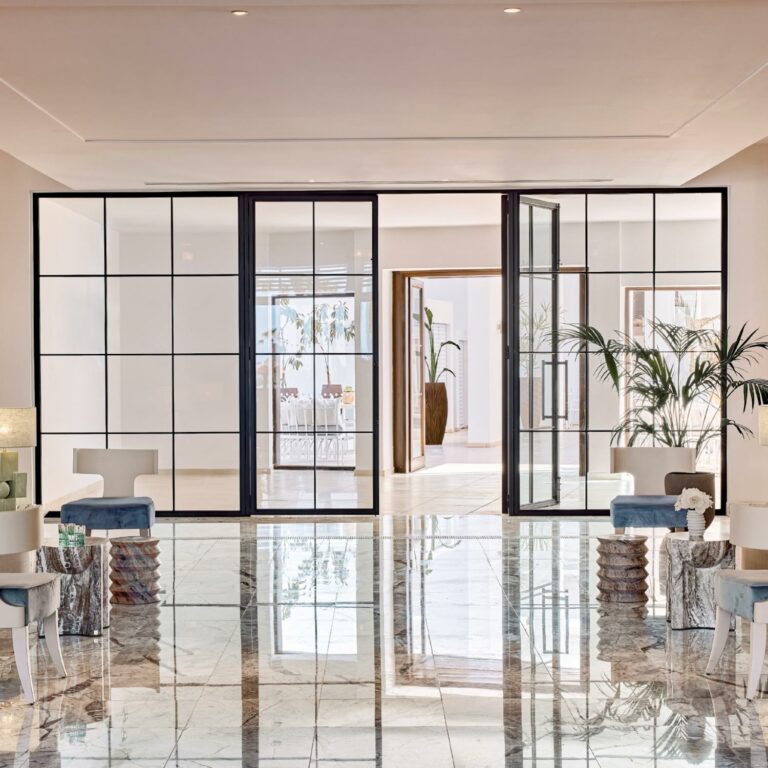Modern lobby with glass partitions, marble floors, and minimalist seating.