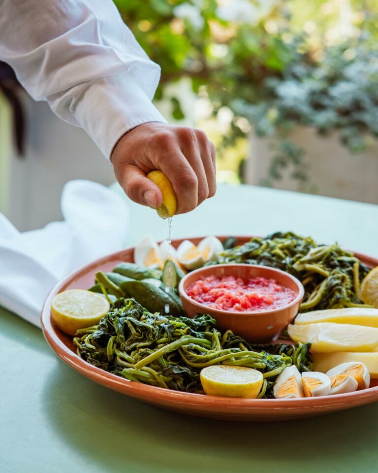 Fresh Cretan greens served with lemon wedges, vegetables and dipping sauce on a rustic table.