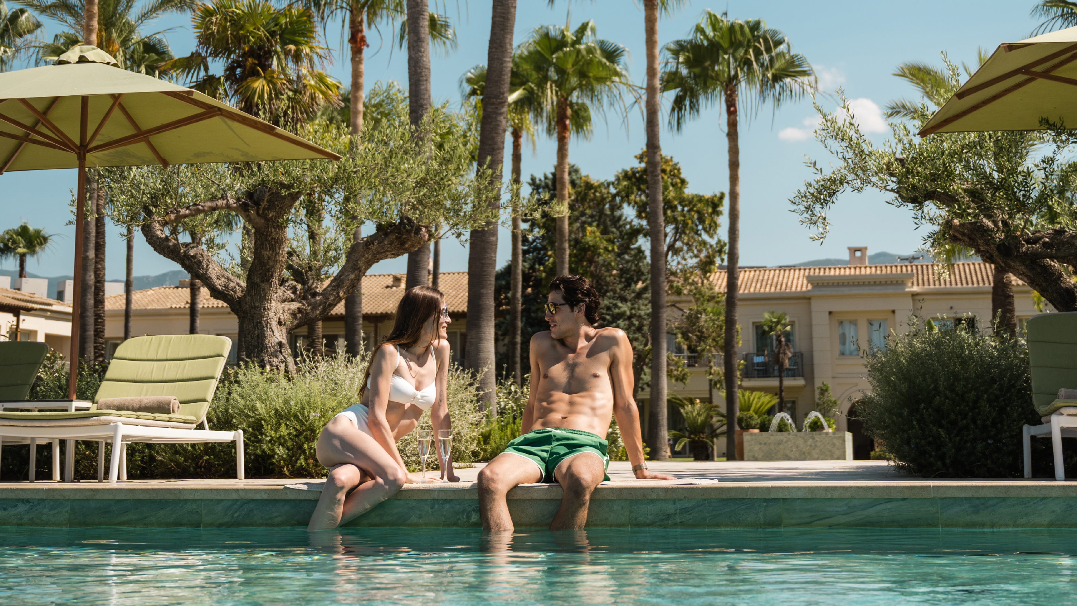 Couple relaxing by the outdoor pool surrounded by palm and olive trees