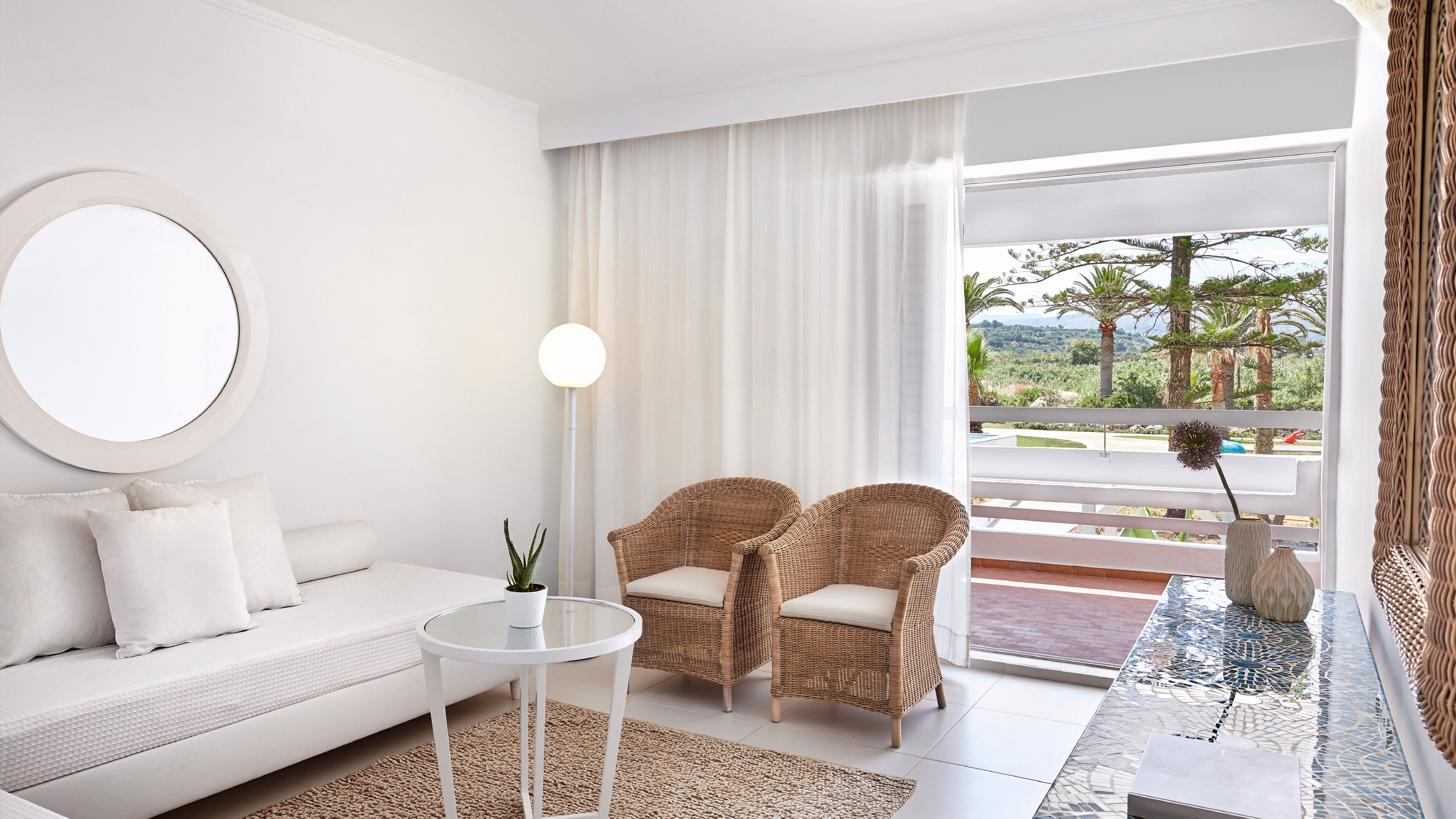 Grecotel LUXME White Crete Family Apartment living area with wicker chairs and garden view.