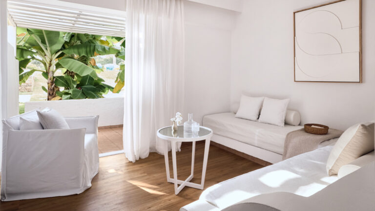 Grecotel LUXME White Crete Family Guestroom living area with sofa, armchairs and garden view.