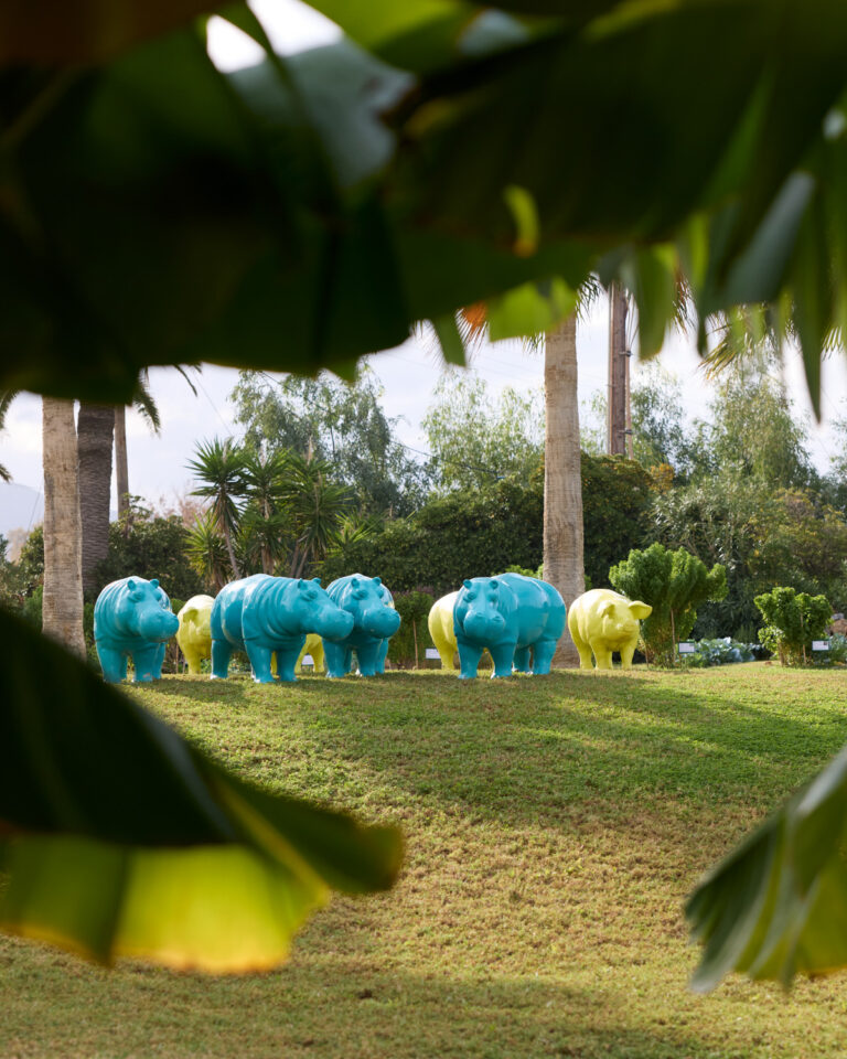 Grecotel LUXME White Crete garden with colourful hippo sculptures and palm trees.