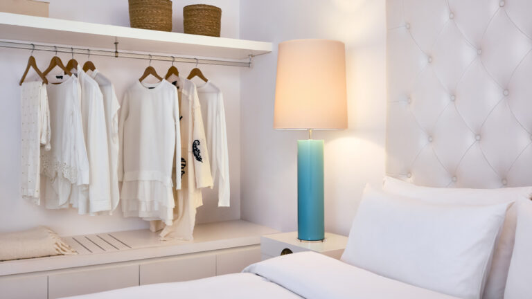 Grecotel LUXME White Crete Petit Yali Seafront Suite bedroom with open wardrobe and bedside lamp.