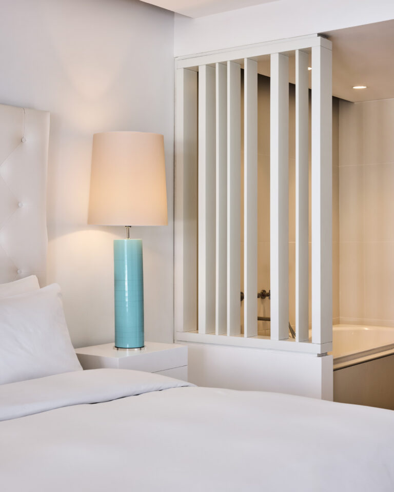Grecotel LUXME White Crete Yali Seafront Suite bedroom with bedside lamp and bathtub.
