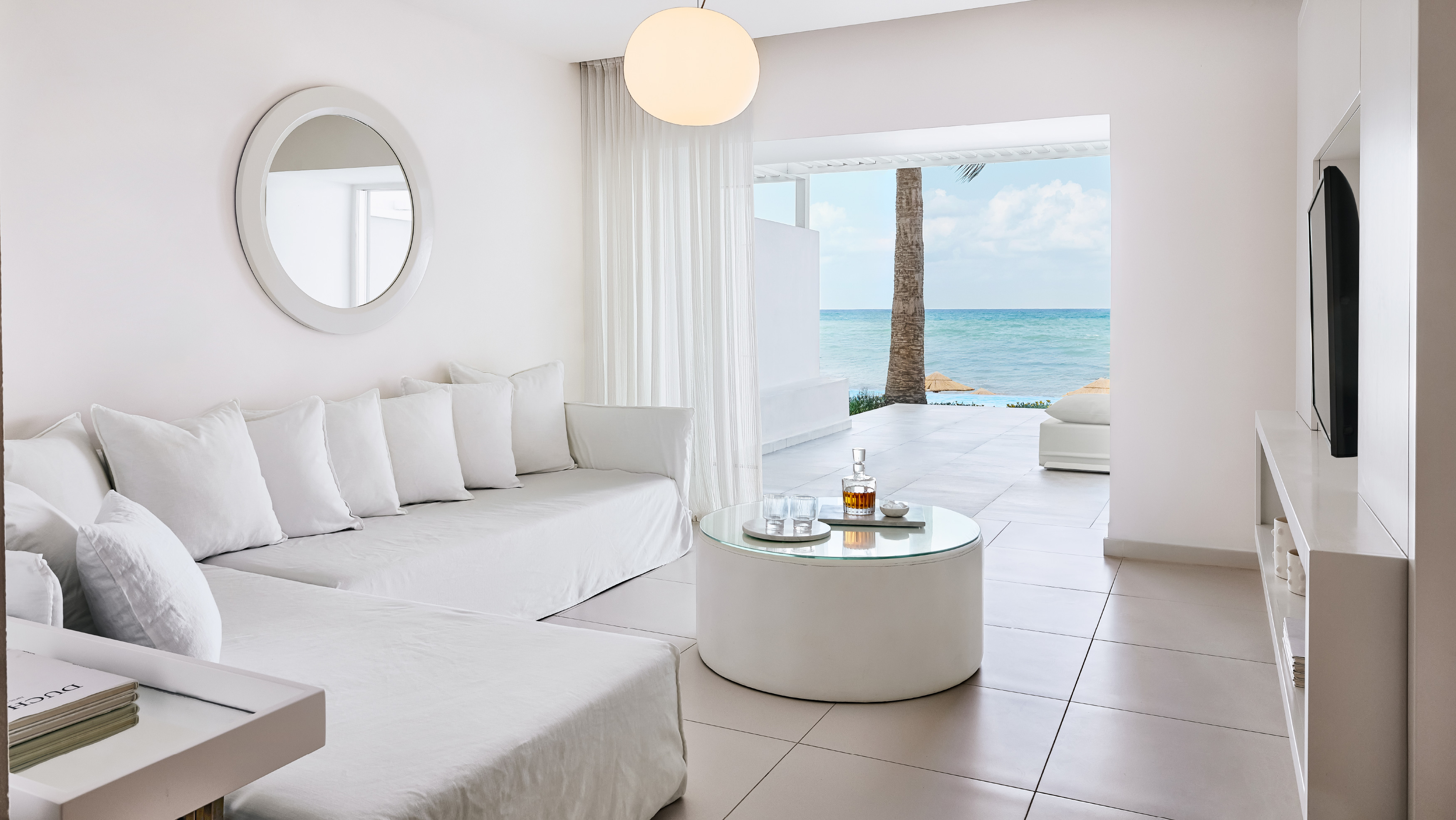 Grecotel LUXME White Crete Yali Seafront Suite living area with sofa, coffee table and sea view.