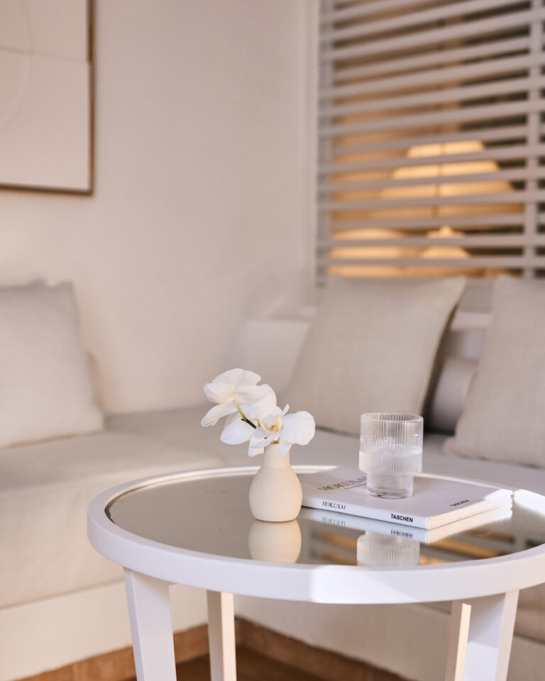 Grecotel LUXME White Crete Family Guestroom seating area with flowers, glass and books.