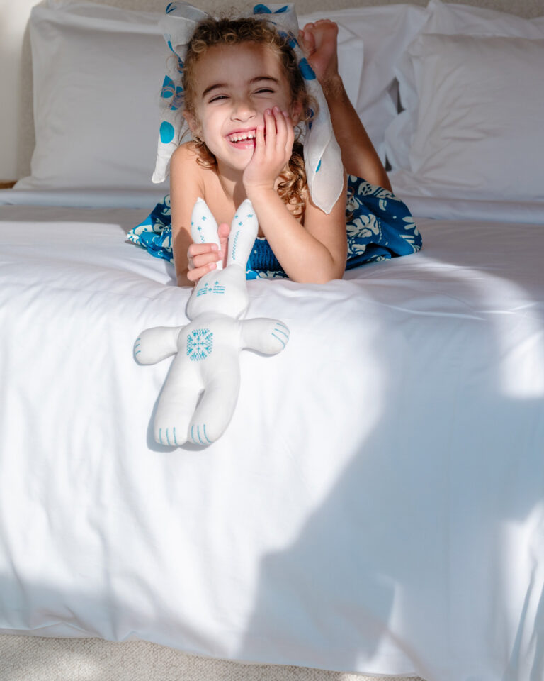 Child relaxing on the bed with a soft toy in a Grecotel LUXME White Crete Grand Family Suite.