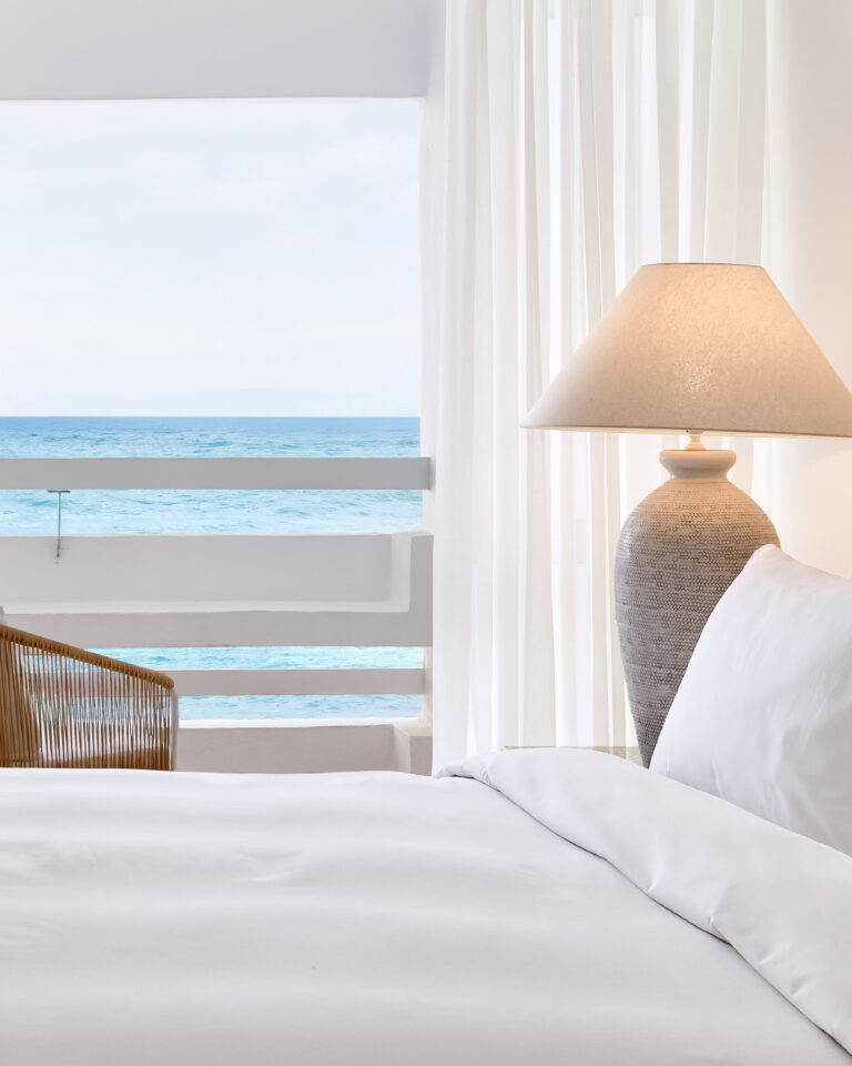 Grecotel LUXME White Crete White Suite bedroom with sea view and bedside lamp.