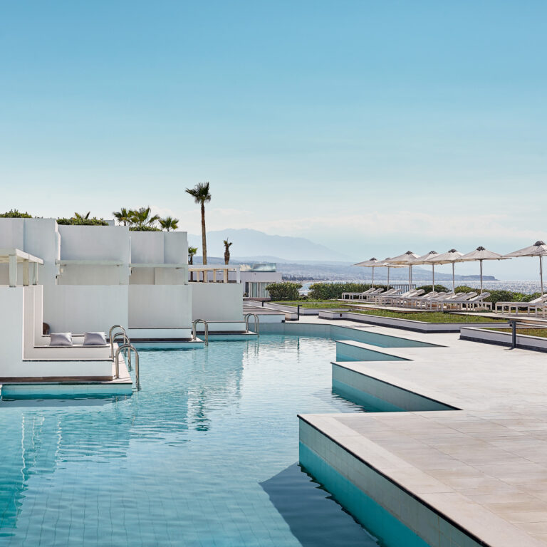 Grecotel LUXME White Crete swim-up pools with sunbeds, sea views and mountain backdrop.