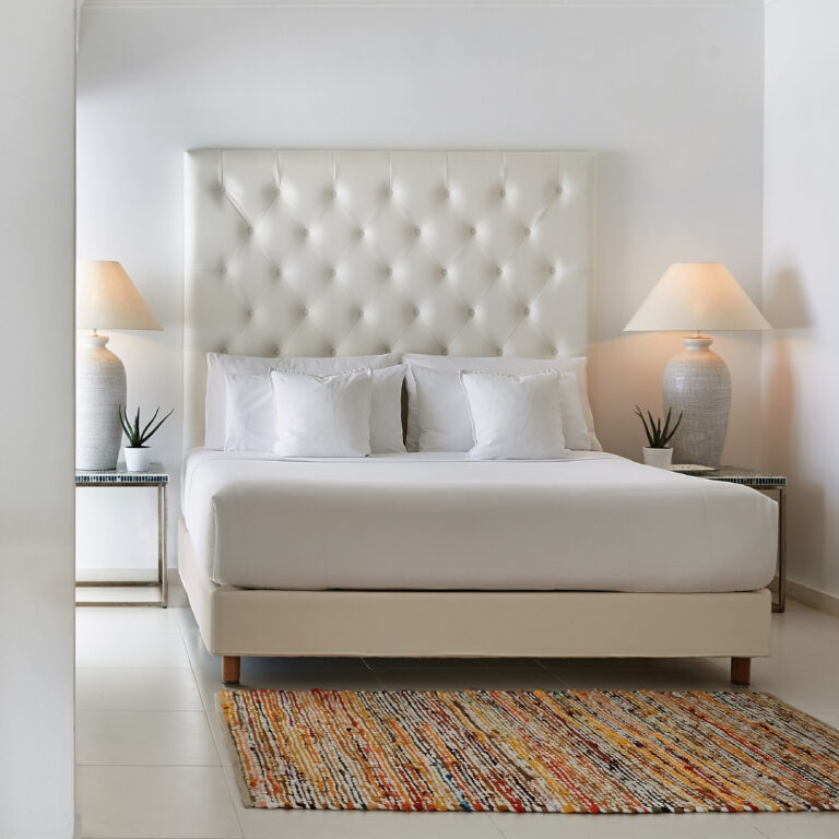 Grecotel LUXME White Crete White Family Suite king bed with upholstered headboard and bedside lamps.