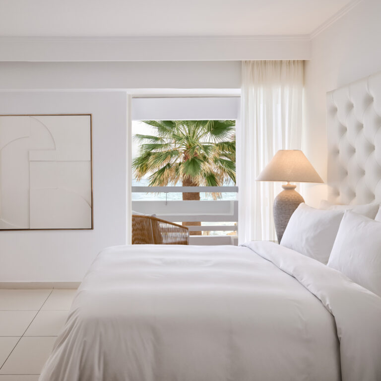 Grecotel LUXME White Crete White Suite bedroom with palm tree and sea view.