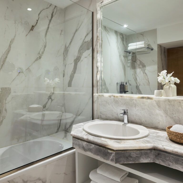 Grecotel LUXME White Crete Swim-up Family Guestroom bathroom with marble vanity and glass shower.
