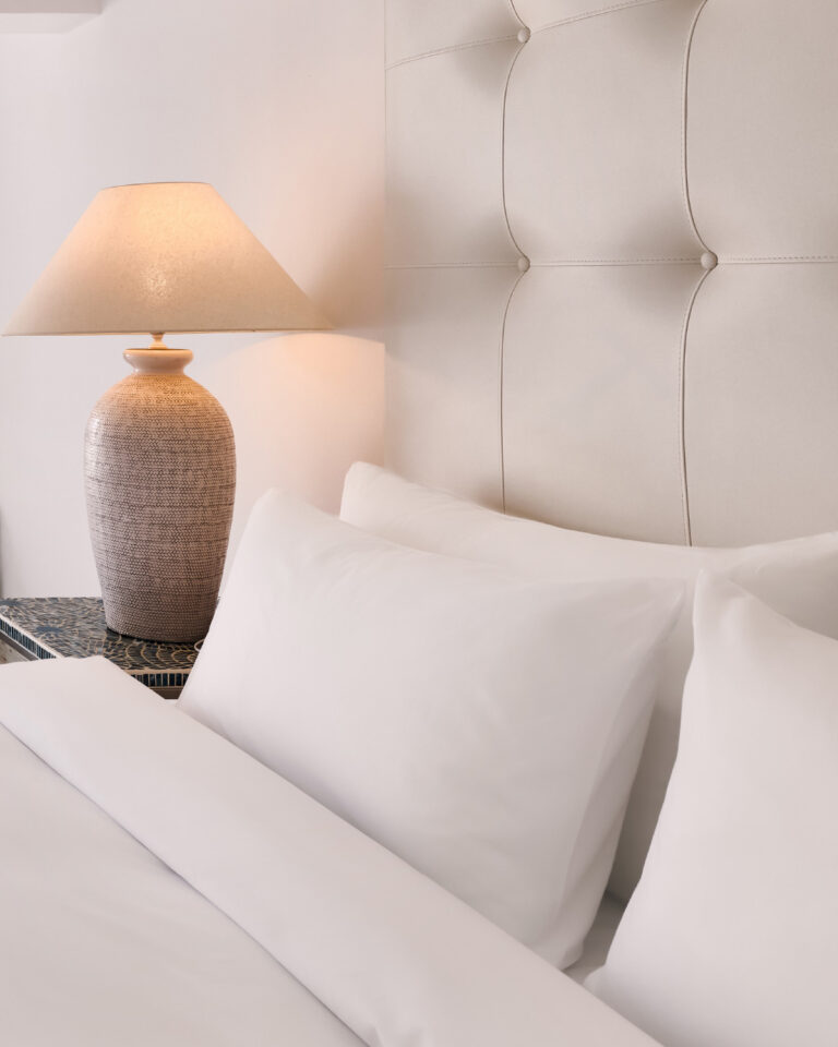 Grecotel LUXME White Crete Open-plan Suite bedroom with upholstered headboard and bedside lamp.