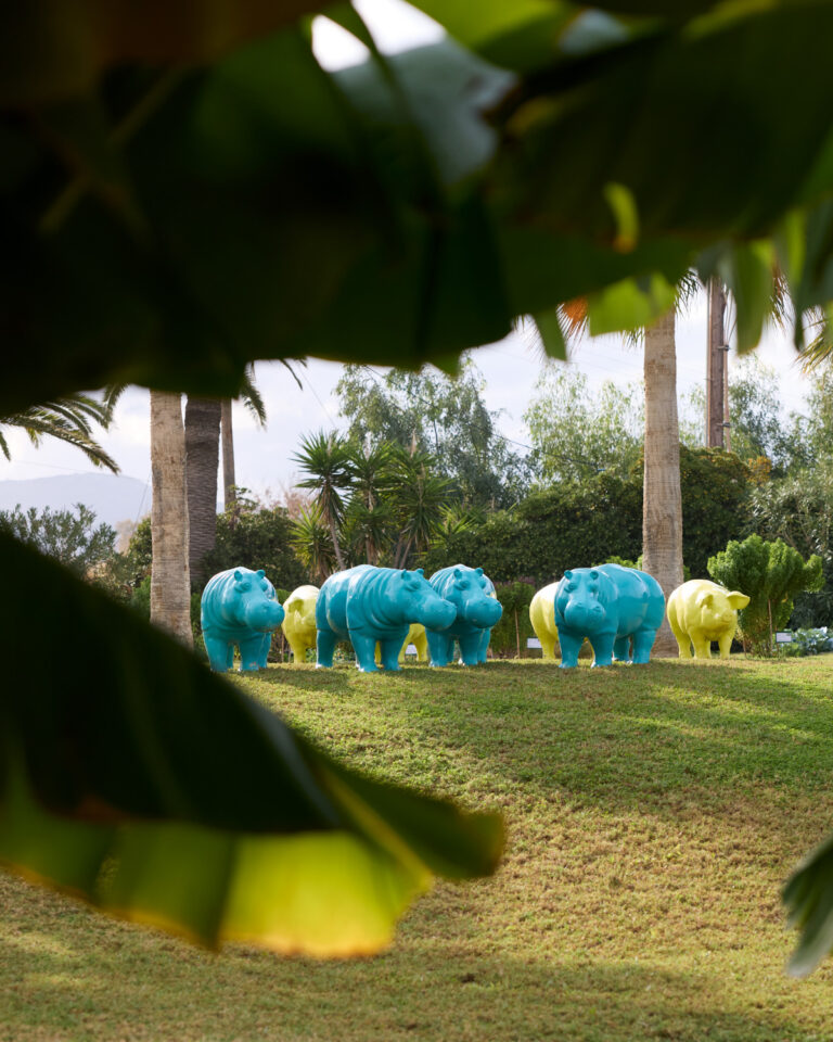 Grecotel LUXME White Crete garden with colourful hippo sculptures and palm trees.