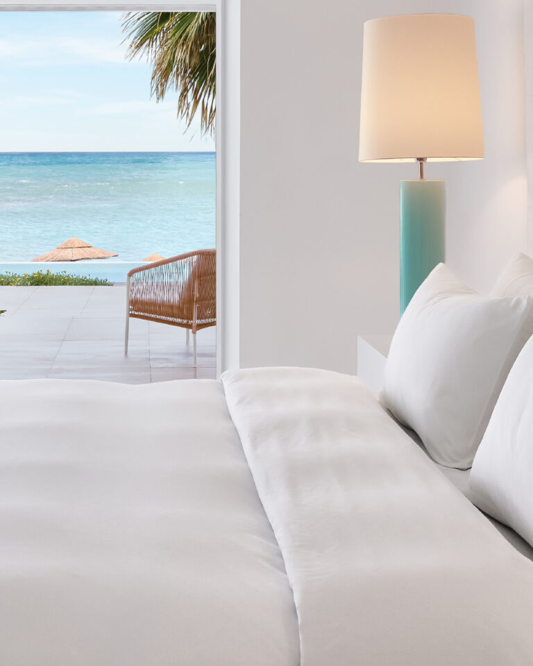 Grecotel LUXME White Crete Yali Seafront Suite bedroom with sea view and turquoise bedside lamp.
