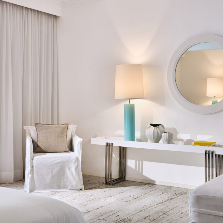 Grecotel LUXME White Crete Junior Suite seating area with armchair, console and mirror.
