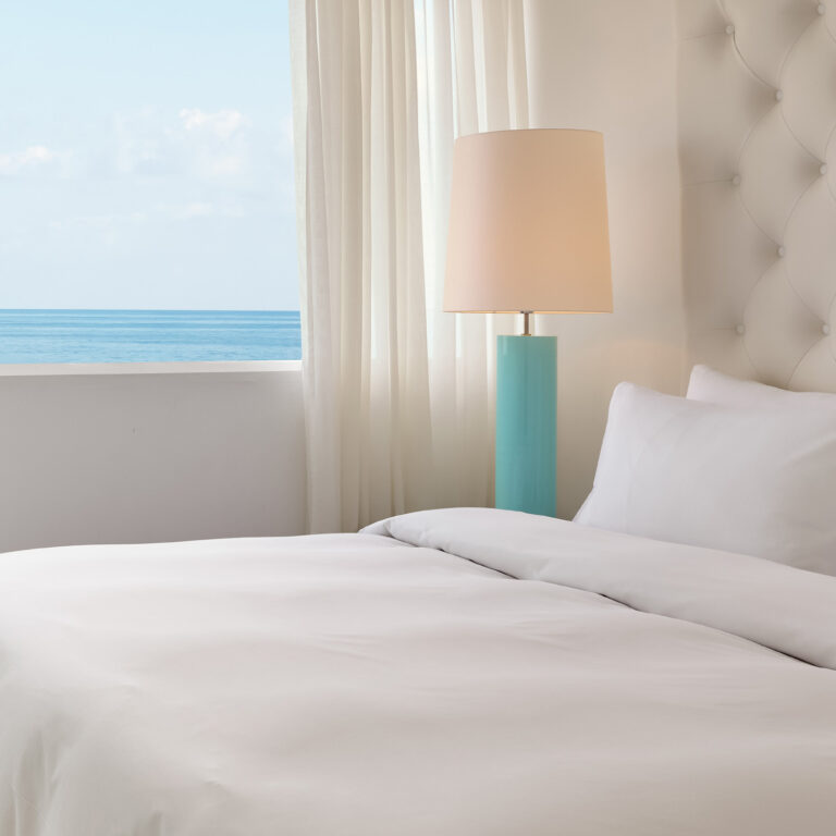 Grecotel LUXME White Crete Grand Family Suite bed with sea view and turquoise bedside lamp.