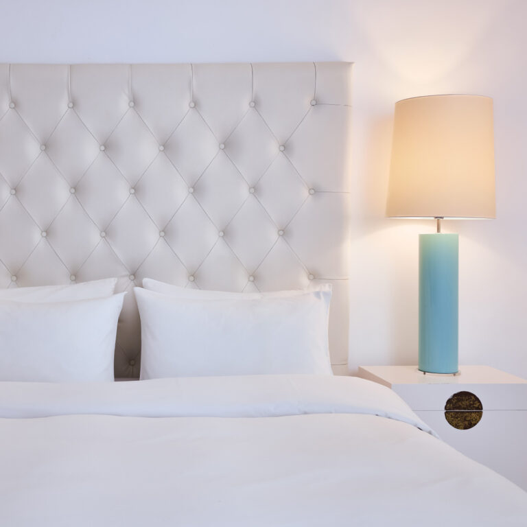 Grecotel LUXME White Crete Petit Yali Seafront Suite bedroom with white upholstered headboard and bedside lamp.