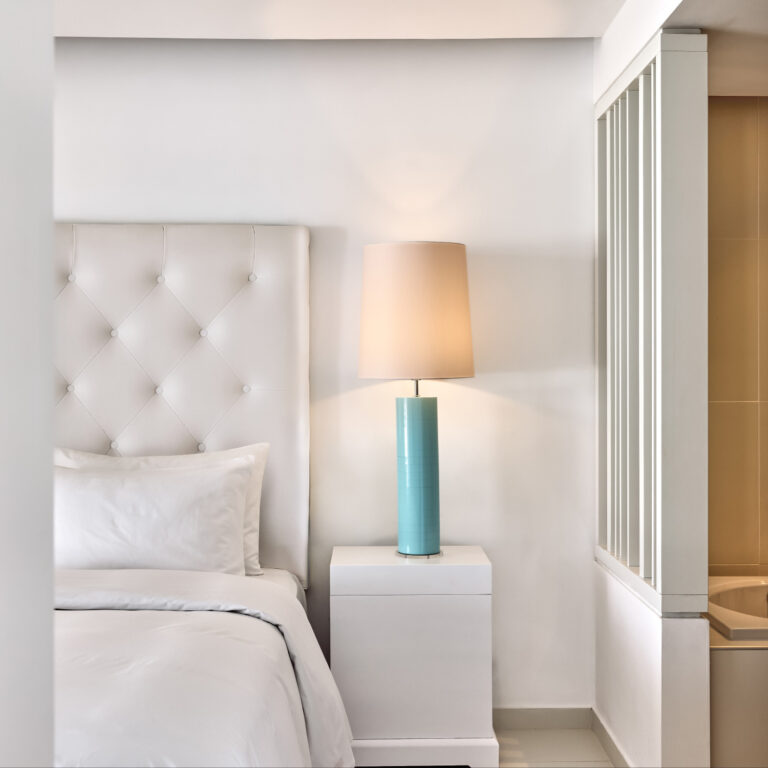 Grecotel LUXME White Crete Yali Seafront Suite bedroom with upholstered headboard and turquoise lamp.