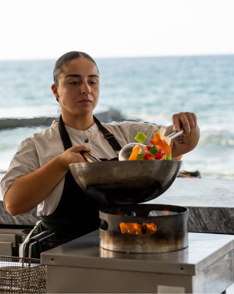 Chef preparing vegetables in a pan overlooking the sea at Grecotel LUXME White Crete.