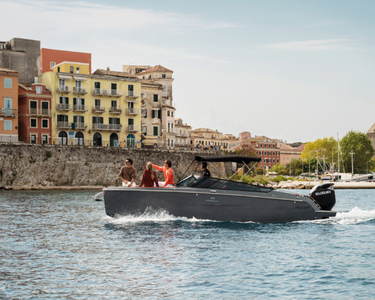 People enjoying a motorboat ride along the colorful waterfront of Corfu Town on a sunny day.